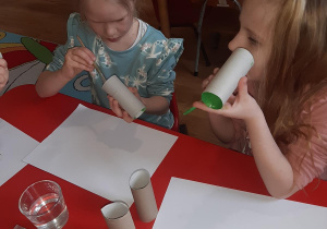 Nikola i Kornelka malują tubki po papierze na zielono aby zrobić z nich liście.