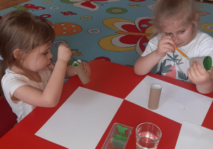 Blanka i Zuzia malują tubki po papierze na zielono aby zrobić z nich liście.
