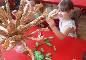 Kuba i Lilka przyklejają liście do gałęzi drzewka.