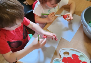 Julek i Marysia malują zakrętki od butelki na czerwono co ma służyć jako jabłuszka.