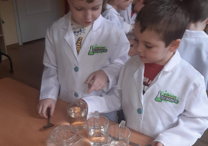 Olek i Witek zmieniają poziom wody w szklankach by sprawdzić jak to wpłynie na wydawany przez nie dźwięk.