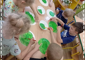 Dzieci malują zieloną farbą talerzyki papierowe