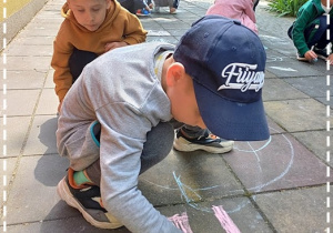 Chłopcy rysują kredą po płycie chodnikowej