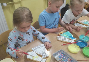 Dzieci dekorują lukrem ciastko w kształcie sukienki i krawata.