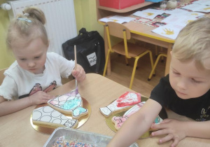 Dzieci dekorują lukrem ciastko w kształcie sukienki i krawata.