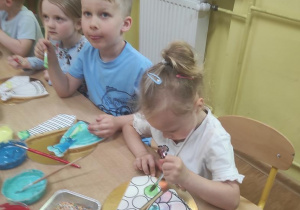 Dzieci dekorują lukrem ciastka w kształcie sukienki i krawata.