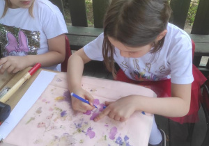 Dzieci układają na tkaninie kompozycje z kwiatów i wybijają gumowym młotkiem.