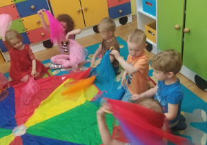 Dzieci siedzą dookoła chusty animacyjnej i ilustrują muzykę za pomocą chust