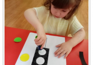 Dziewczynka przykleja kolorowe kółeczka na sygnalizator