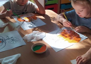 Dzieci malują sylwetę dyni farbami