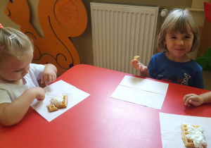 Dzieci jedzą gofry z bitą śmietaną.