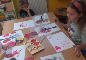 Dzieci malują farbami liście i stemplują nimi sylwetę drzewa