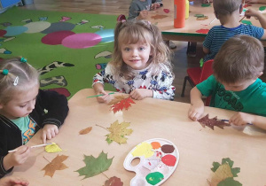 Lenka, Ola i Igor malują liście farbami.