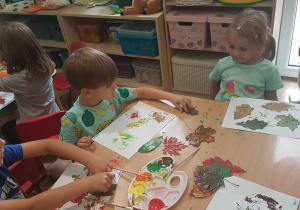Lidia ,Wojtek i Oliwier malują liście farbami.