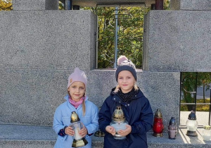 Amelka i Nela ze zniczami pod pomnikiem.