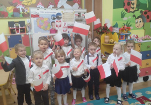 Dzieci - przed występem- stoją na tle dekoracji , w rękach trzymają flagi Polski.