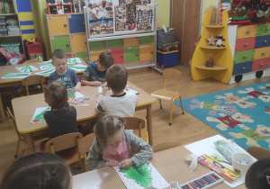 Dzieci kolorują i naklejają ozdoby na choince.