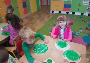 Dzieci malują papierowe talerzyki zieloną farbą.