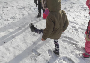 Dzieci robią i oglądają ślady na śniegu.
