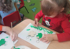 Hania maluje breloczki zieloną farbą.