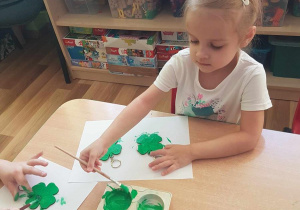 Lidia maluje breloczki zieloną farbą.