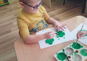 Lucjan maluje breloczki zieloną farbą.