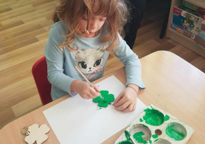 Lenka maluje breloczki zieloną farbą.