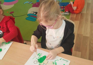 Hania maluje breloczki zieloną farbą.