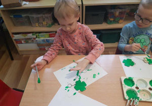 Łucja maluje breloczki zieloną farbą.