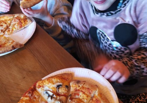 Dzieci jedzą przygotowaną przez siebie pizzę