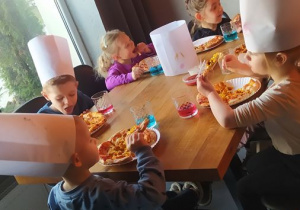 Dzieci jedzą przygotowaną przez siebie pizzę