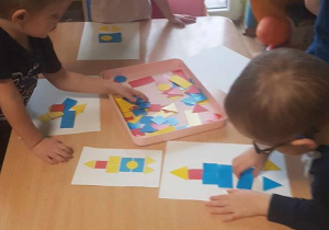 Dzieci przyklejają na karton kompozycję z figur geometrycznych.