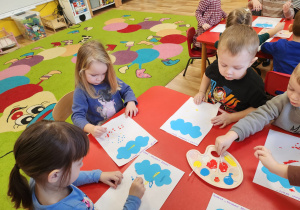 Dzieci wykonują deszcz za pomocą farb i patyczków.