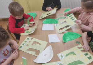 Dzieci wypychają części dinozaura i naklejają na pomalowany talerzyk.