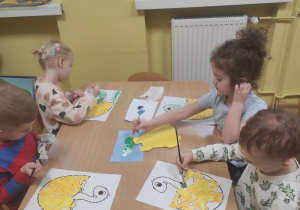 Dzieci wyklejają jajko wydzieranką z kolorowego papieru a dinusia malują farbami plakatowymi.