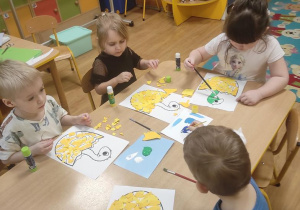 Dzieci wyklejają jajko wydzieranką z kolorowego papieru a dinusia malują farbami plakatowymi.
