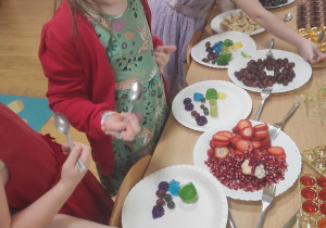Dzieci układają tęczę z galaretek a następnie dokładają owoce w odpowiednich kolorach.