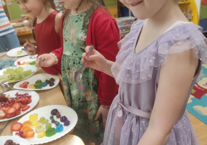 Dziewczynki układają tęczę z galaretek a następnie dokładają owoce w odpowiednich kolorach.