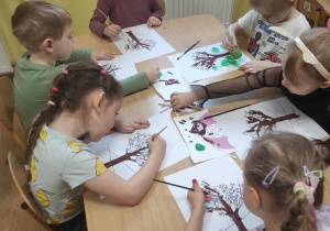Dzieci malują konary drzew.