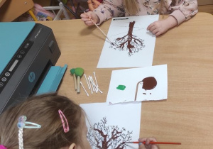 Dziewczynki malują drzewa.