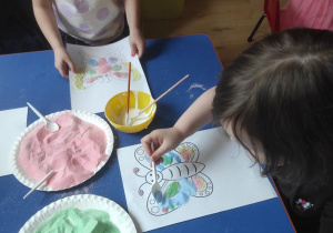Dzieci ozdabiają motyla kolorową solą.