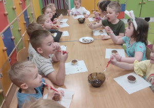 Dzieci ozdabiają babeczki płynna czekoladą i ją próbują.
