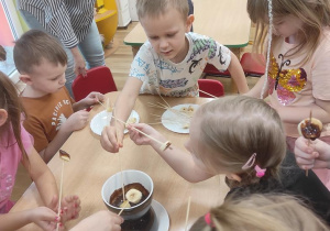 Dzieci maczają owoce w płynnej czekoladzie i je zjadają.