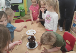Dzieci maczają owoce w płynnej czekoladzie i je zjadają.