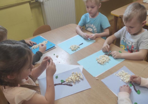 Dzieci przyklejają popcorn i lepią łodygę i liście.