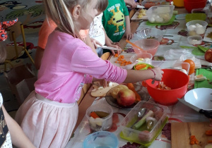 Dzieci stoją przy stolikach i kroją warzywa
