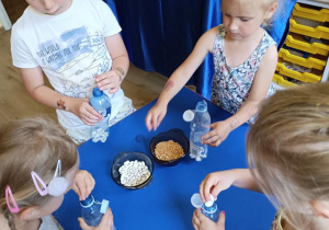 Dzieci wykonują marakasy- napełniają butelki grochem i fasolą.