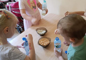 Dzieci wykonują marakasy- napełniają butelki grochem i fasolą.