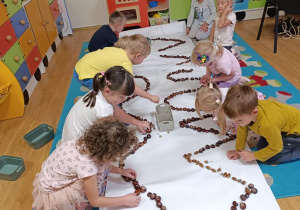 Dzieci układają wzory z kasztanów i żołędzi.