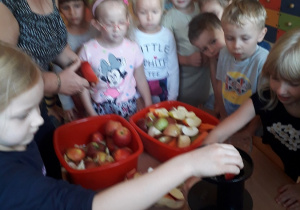 Oliwia wkłada jabłko do wyciskarki, dzieci obserwują.